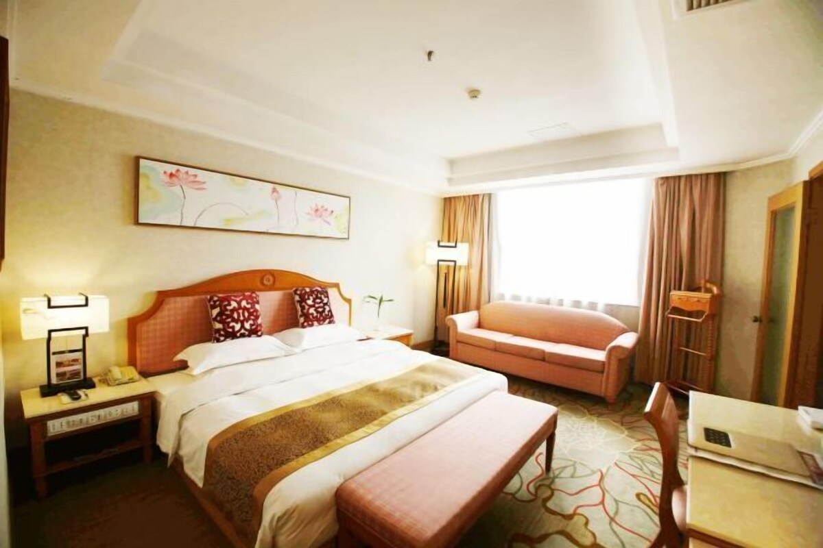A hotel room with a large bed, a sitting area with a sofa, a desk, and a window with curtains.