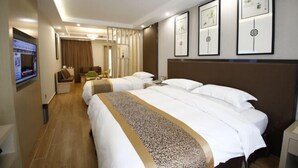 Ein Hotelzimmer mit zwei Betten, einem Fernseher, einem Schreibtisch und gerahmten Kunstwerken an der Wand.
