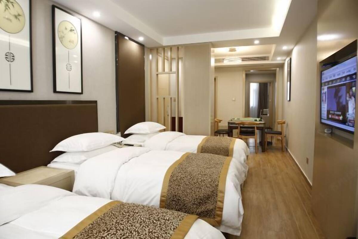 A hotel room with three beds, a desk, a chair, and a television.