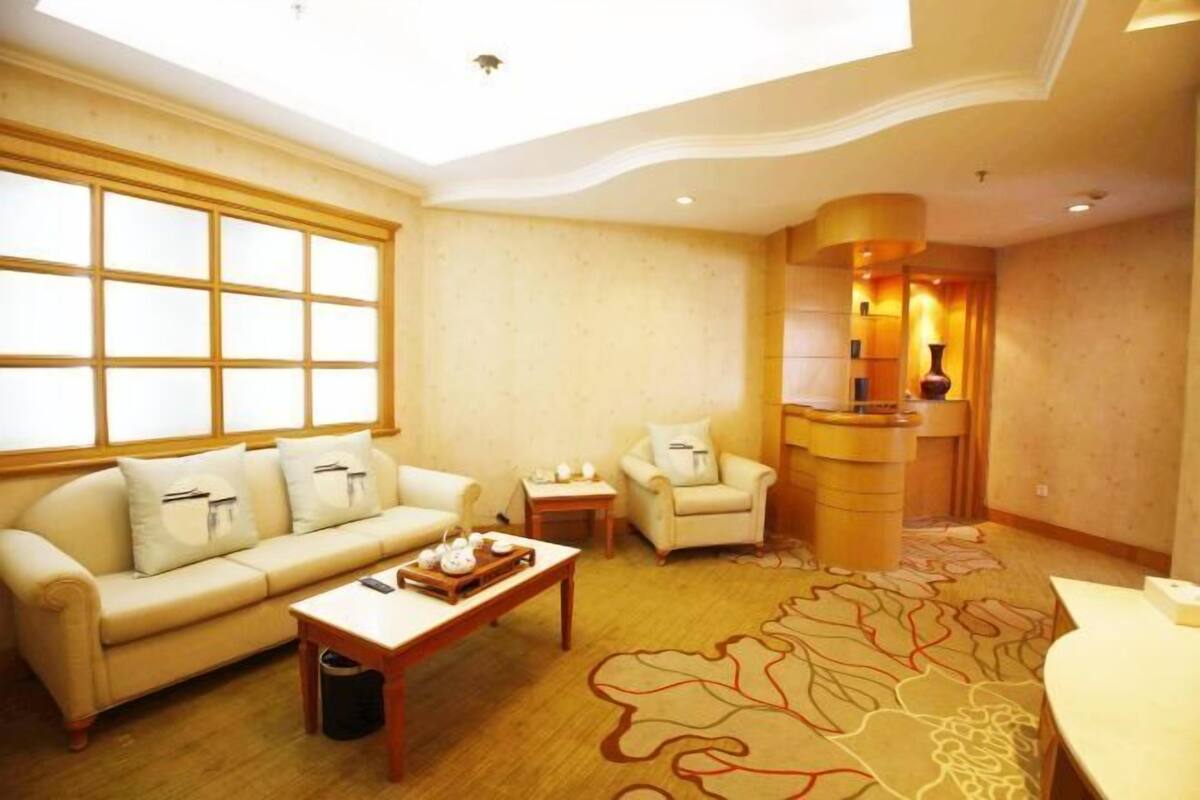A hotel room with a large window, a sofa, a chair, a small table, and a decorative rug.