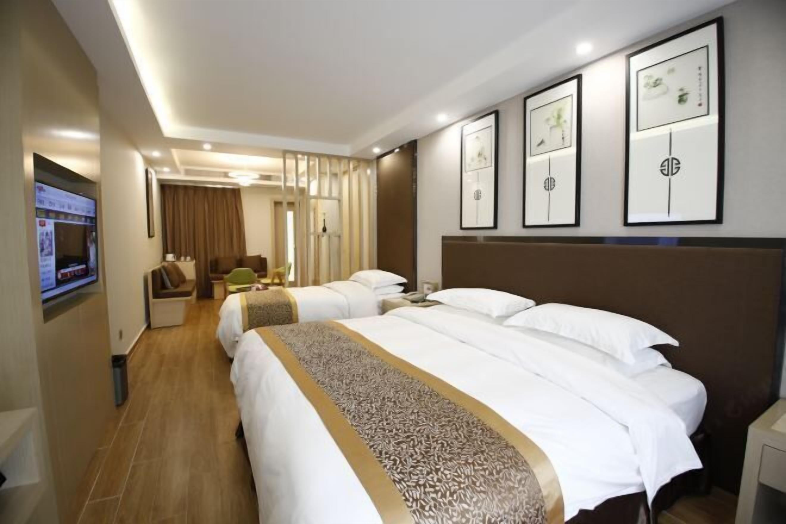 A hotel room with two beds, a TV, a desk, and framed artwork on the wall.