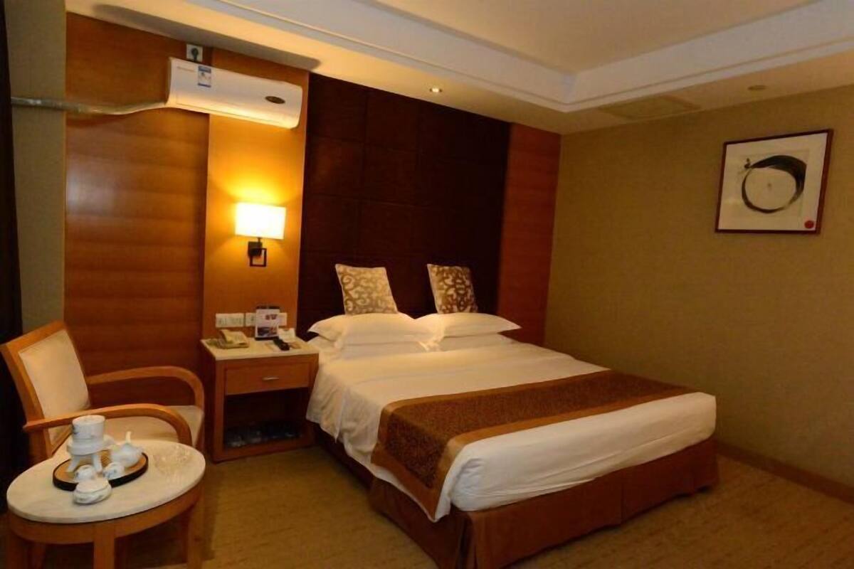 A hotel room with a bed, a chair, a small table with a tray, a nightstand, and a wall-mounted lamp.