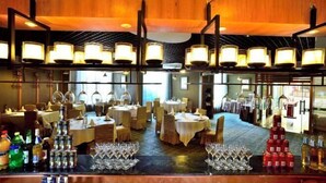 Ein Restaurant mit mehreren Tischen, einer Bar mit Flaschen und Gläsern sowie einer warmen Holzzieldecke.