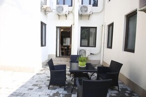 Un patio con mesa y sillas, una planta en maceta y equipos de aire acondicionado en la pared.
