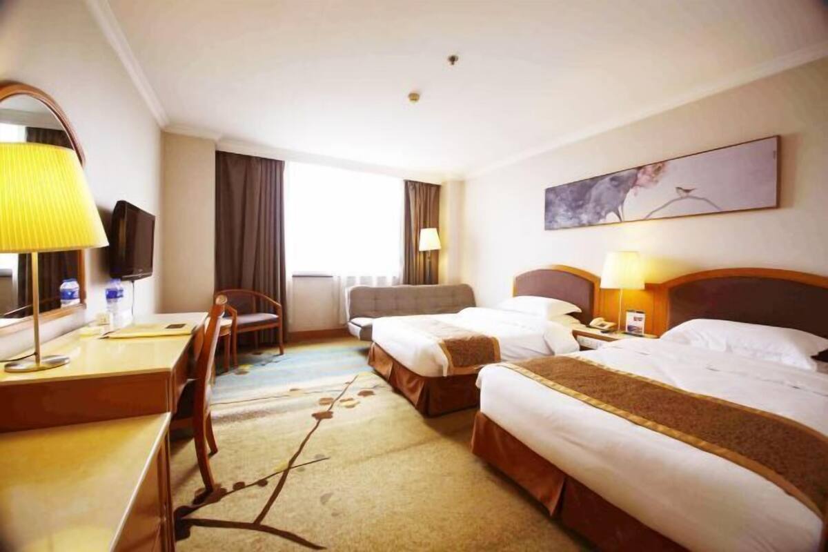 A hotel room with two beds, a desk, a chair, a TV, and a window with curtains.