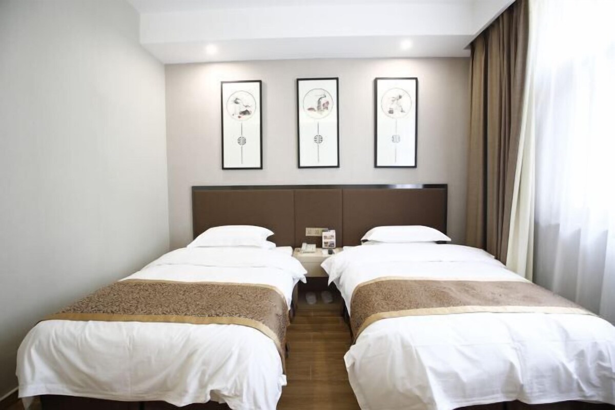A hotel room with two beds, a headboard, a nightstand, and three framed pictures on the wall.