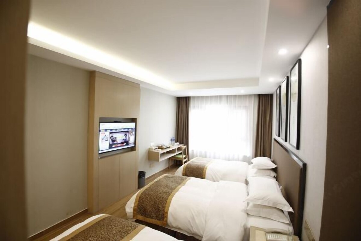 A hotel room with two beds, a TV, a desk, and a window with curtains.