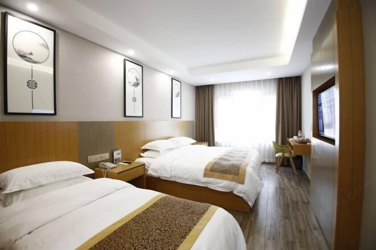 A hotel room with two beds, a desk, a chair, and a window with curtains.
