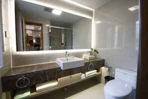 Un baño moderno con un espejo grande, un lavamanos blanco, un inodoro y un tocador de mármol con toalleros.