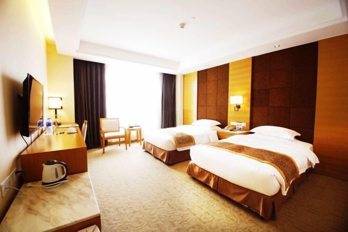A hotel room with two beds, a desk with a kettle, a chair, and a TV.