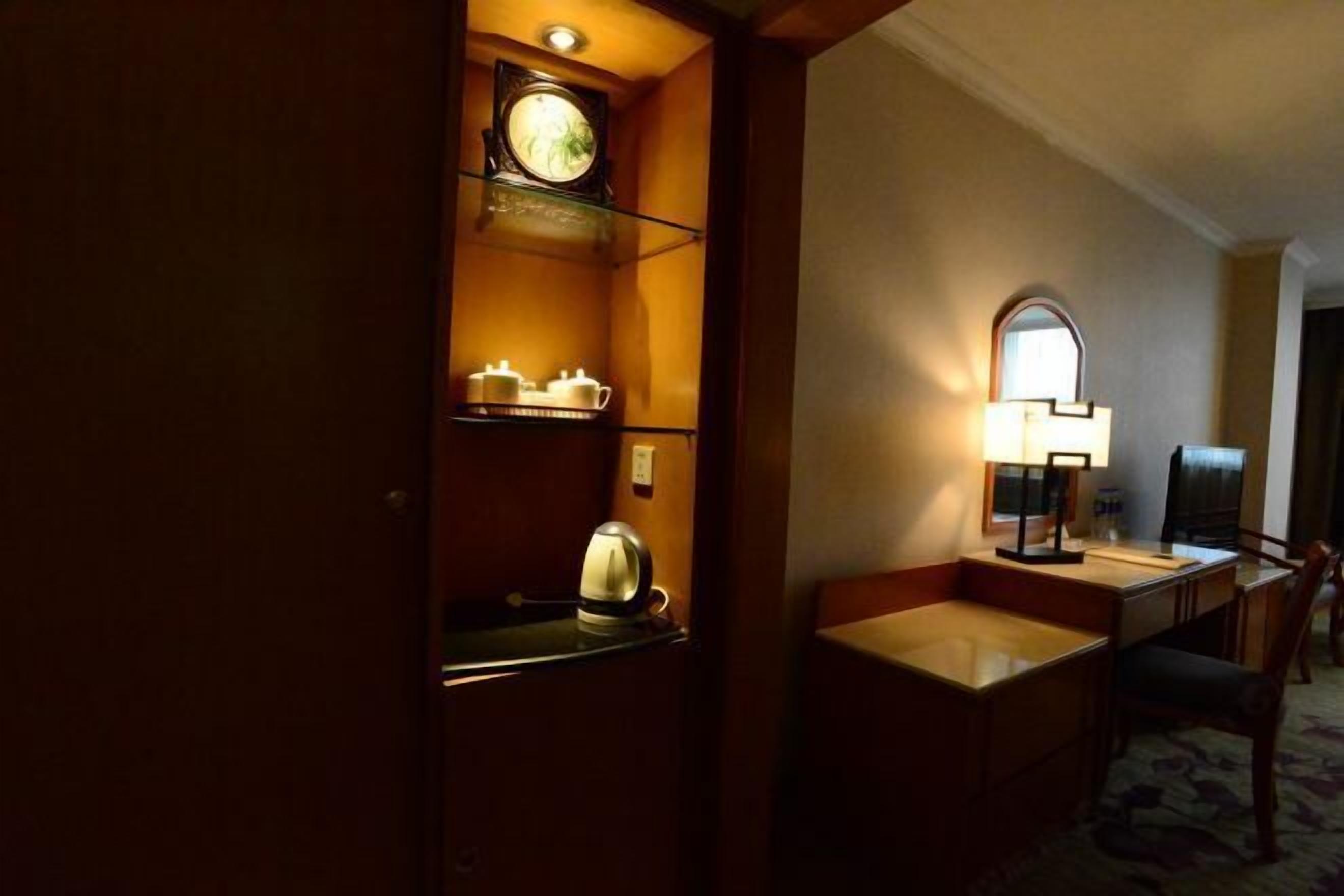 Una habitación de hotel con un escritorio de madera, una lámpara, un reloj y un espejo.