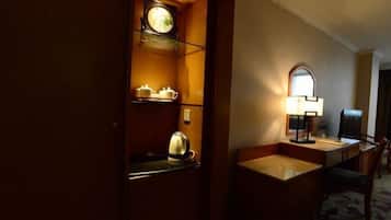 Una habitación de hotel con un escritorio de madera, una lámpara, un reloj y un espejo.