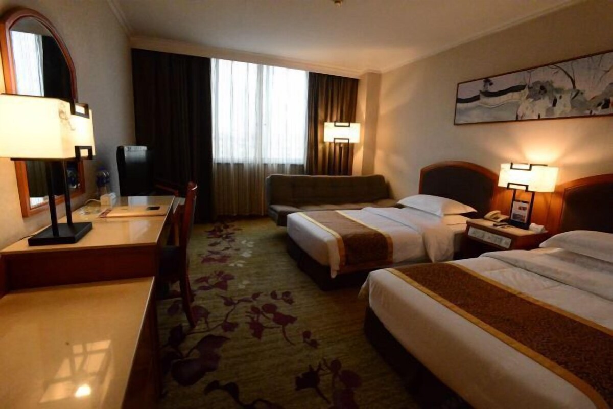A hotel room with two beds, a desk, a chair, a TV, and a window with curtains.