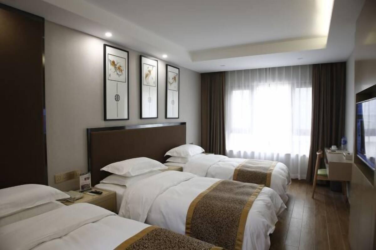 A hotel room with three beds, a desk, a TV, and framed artwork on the wall.