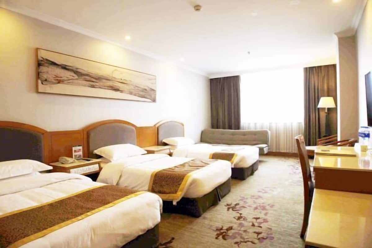 A hotel room with two beds, a desk, a chair, a lamp, and a painting on the wall.