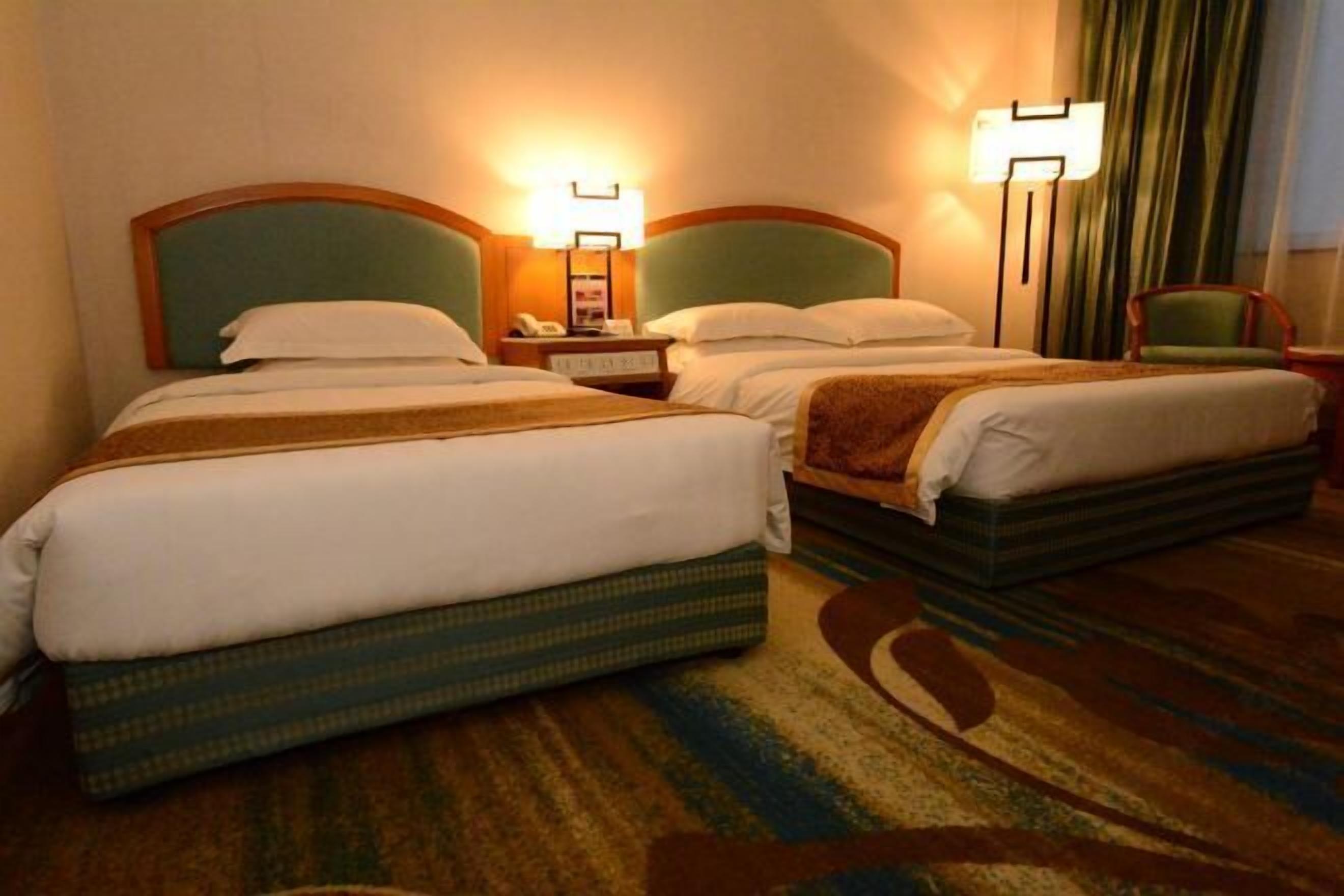 Une chambre d’hôtel avec deux lits, chacun doté d’une tête de lit, de tables de chevet, de lampes et d’un sol recouvert de moquette.