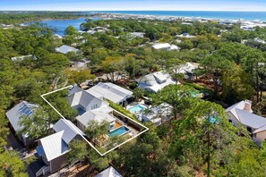 An aerial view of a residential area with houses, a swimming pool, and a beach in the background.