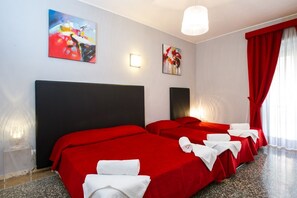 A hotel room with two beds, red bedding, white towels, abstract art on the walls, and a red curtain.