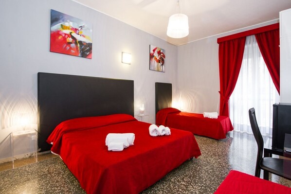 A hotel room with two beds, red bedding, artwork on the walls, and a red curtain.