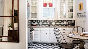 A kitchen with white cabinets, a black and white tiled floor, a round wooden table, and a stained glass window above the sink.