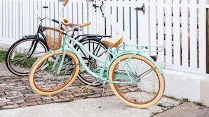 A house with a porch, a white picket fence, and two bicycles parked in front.