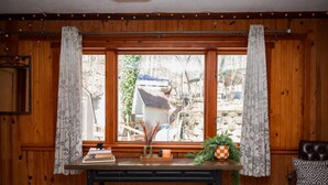 A wooden-paneled room with a large window, a bench, a leather chair, and a small table with books and a plant. - Lakefront  Hot tub. Amazing views. 35 min to Indy (Martinsville)