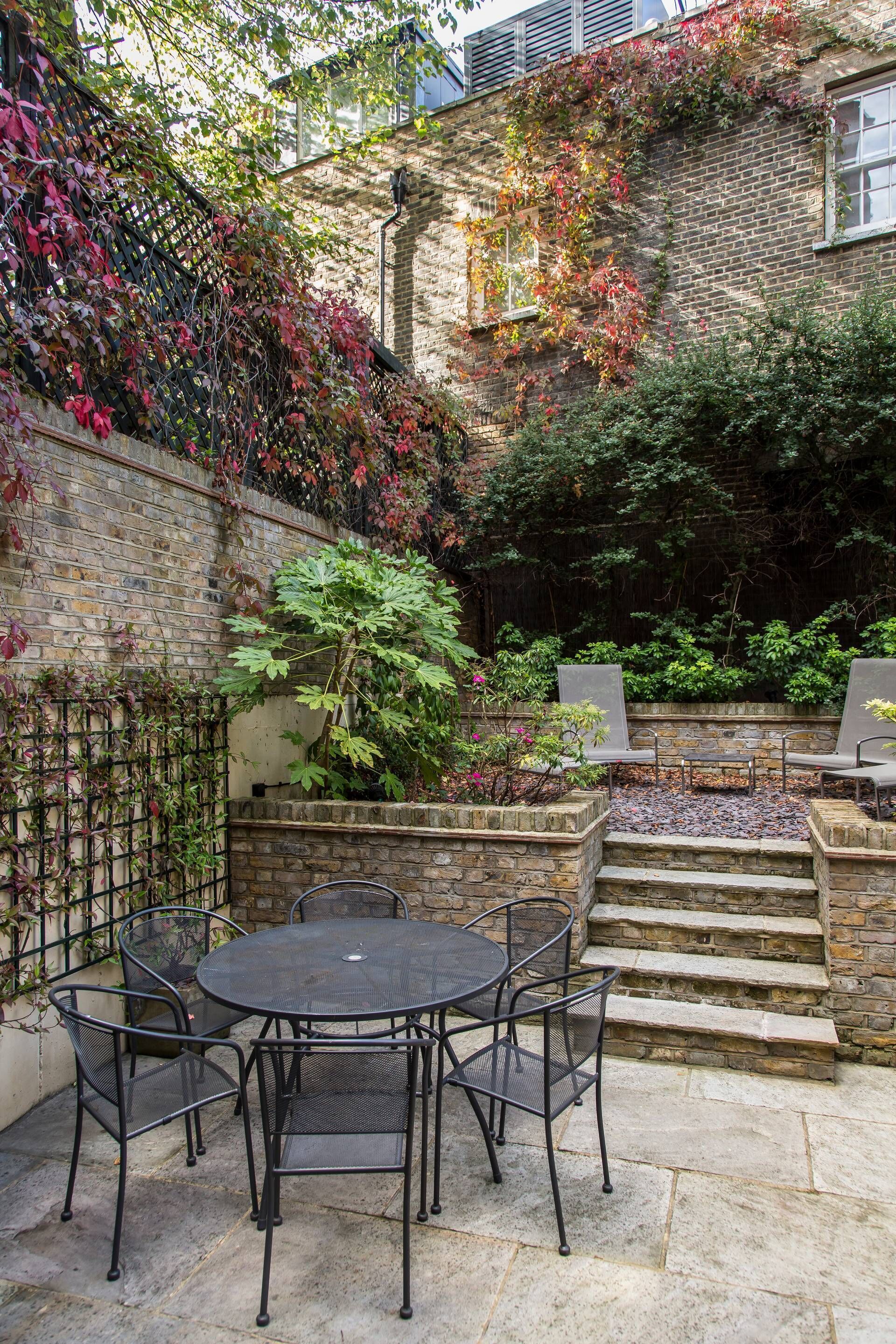 A patio with a round table and chairs, surrounded by stone steps and a brick wall.