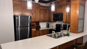 A kitchen with wooden cabinets, a stainless steel refrigerator, a microwave, and a sink with a faucet. - Supérieur HBC themed condo in Tremblant village (Mont-Tremblant)
