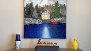 A painting of a house by a lake with a boat, a blue vase, and a yellow vase on a table. - Supérieur HBC themed condo in Tremblant village (Mont-Tremblant)