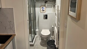A compact bathroom with a glass-enclosed shower, a toilet, and a sink. - Apartment Gutenberg 3 (Paris)