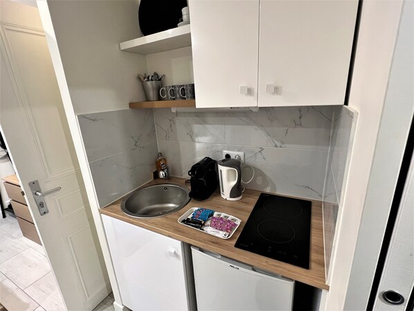 Une cuisine compacte équipée d’un évier, d’une machine à café, d’une bouilloire et d’un petit réfrigérateur.