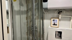 A glass-enclosed shower with a digital control panel, a framed picture of the Eiffel Tower, and a small ventilation grille. - Apartment Gutenberg 3 (Paris)