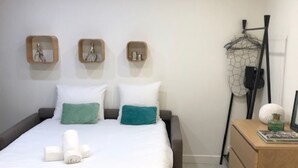 A neatly made bed with white and teal pillows, a wooden bedside table with a framed picture, and a wall-mounted rack with hooks. - Apartment Gutenberg 3 (Paris)