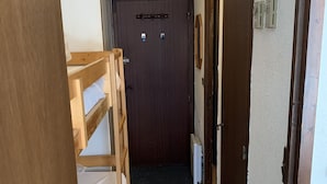 Un couloir étroit, avec des lits superposés sur le côté gauche, une porte au fond et un radiateur sur le côté droit.
