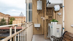 A balcony with a view of a dome building, a water heater, an air conditioning unit, and a bench. - Domus Fabiola Vaticano Matrimoniale (Roma)