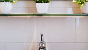 A bathroom with a glass shelf above a white tiled wall, holding three white potted plants. - Domus Fabiola Vaticano Matrimoniale (Roma)