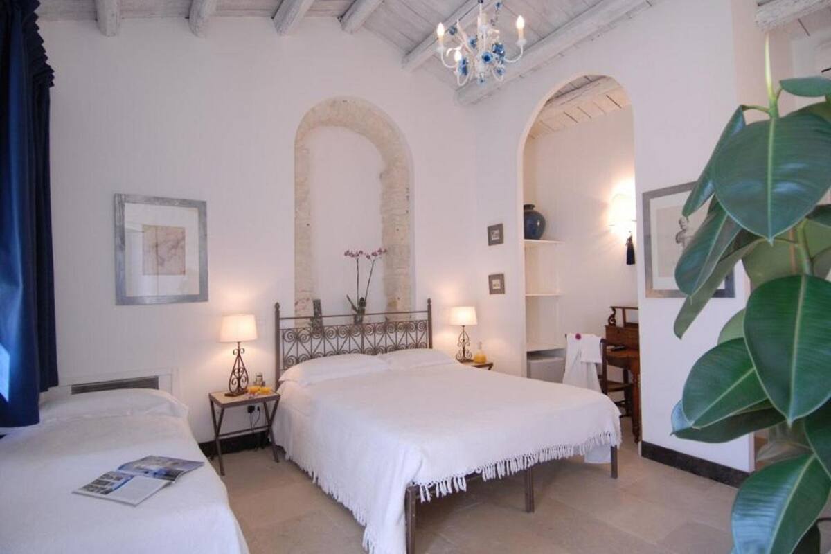 Een hotelkamer met twee bedden, een kroonluchter, een grote plant en een stenen boog.