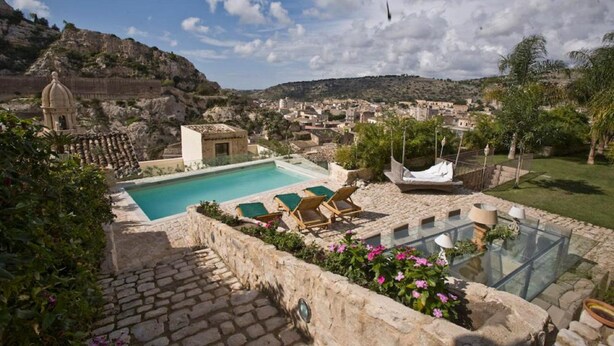 Un espace piscine aménagé avec des chaises longues, une table en verre et une vue sur la ville et les montagnes.