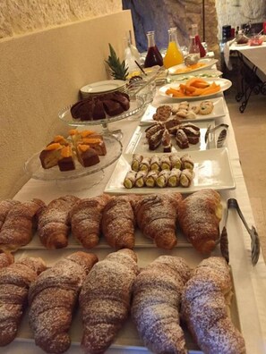En buffet med forskellige kager og desserter, herunder croissanter og andre bagværk.