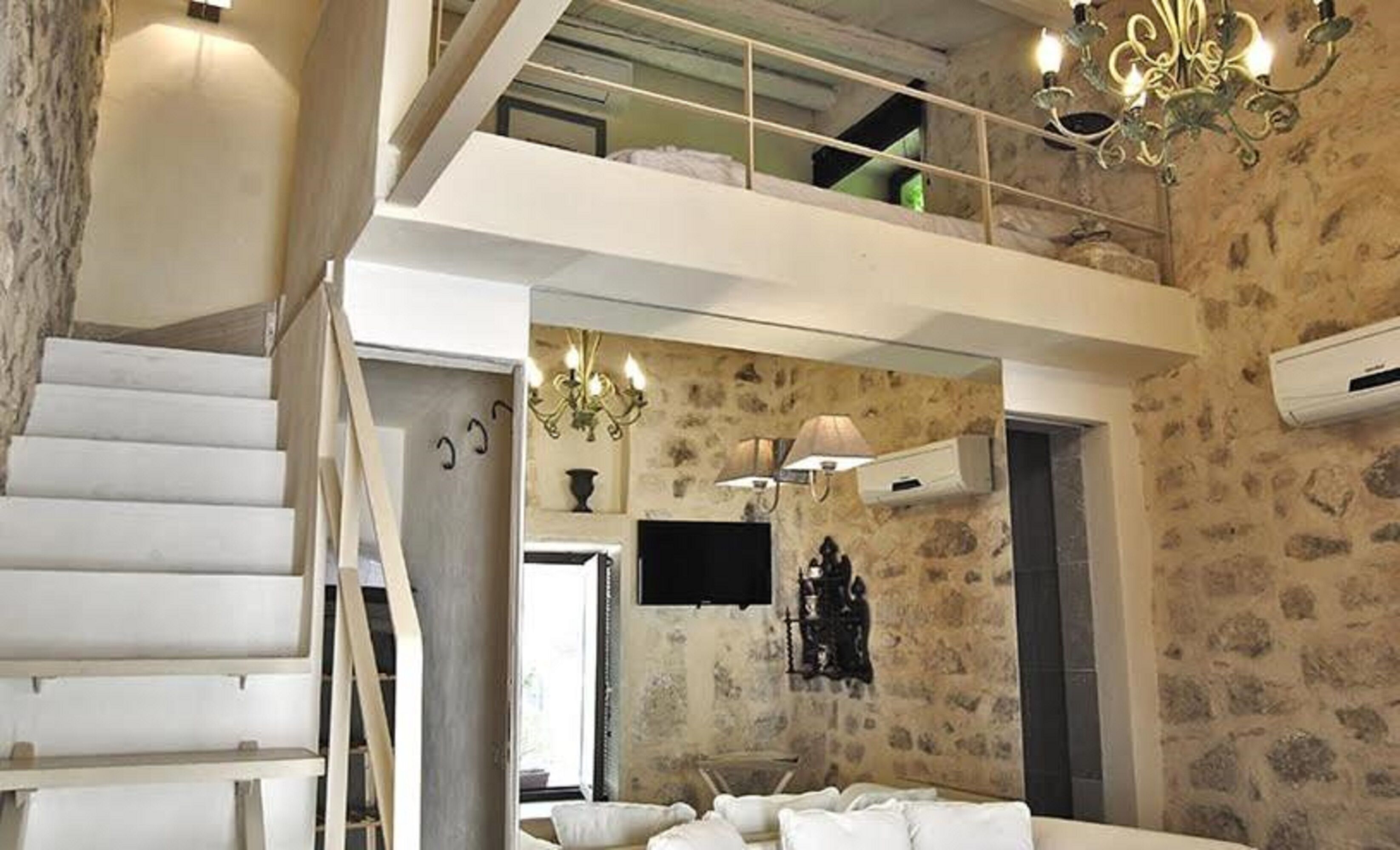 Ein Hotelzimmer mit Steinwand, einer Kandelaber, einem Flachbildfernseher, einem Bett und einer Treppe.