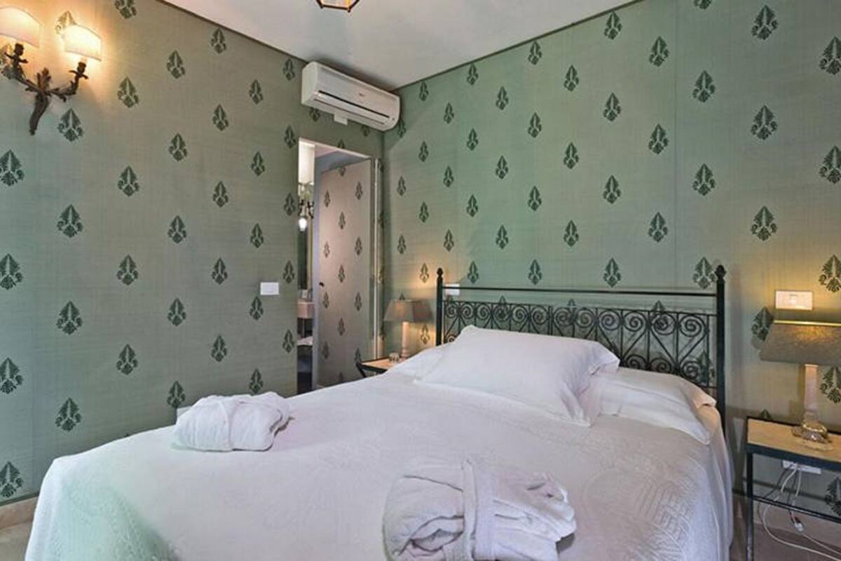 Een hotelkamer met een bed, nachtkastje, lamp en een wandairconditioner.
