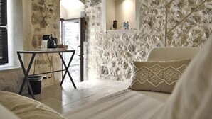 Une pièce chaleureuse avec un mur en pierre, une petite table avec une lampe et un lit agrémenté d’oreillers à motifs.