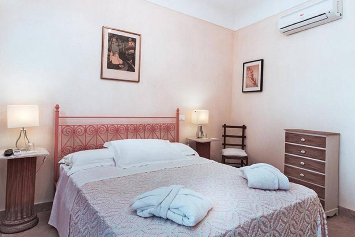 Een slaapkamer met een bed, twee nachtkastjes met lampen, een houten dressoir en twee ingelijste foto's aan de muur.