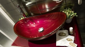 Ein rotes Waschbecken mit einem Chrom-Armaturen, ein kleiner Blumentopf und eine Ablage mit Taschentüchern und einer Karte.