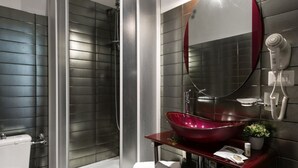 Ein modernes Badezimmer mit einer Duschkabine aus Glas, einem roten Waschtischbecken und einem an der Wand montierten Föhn.