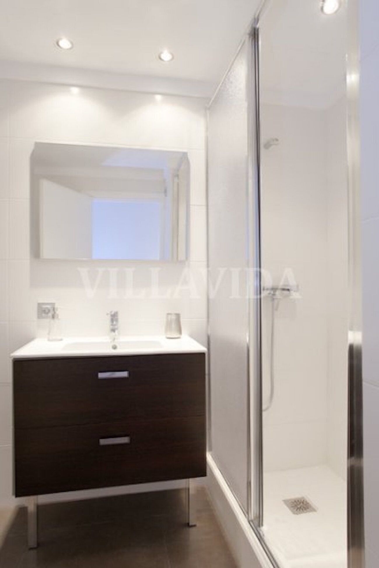 A modern bathroom with a dark wooden vanity, a glass shower enclosure, and a large mirror above the sink.