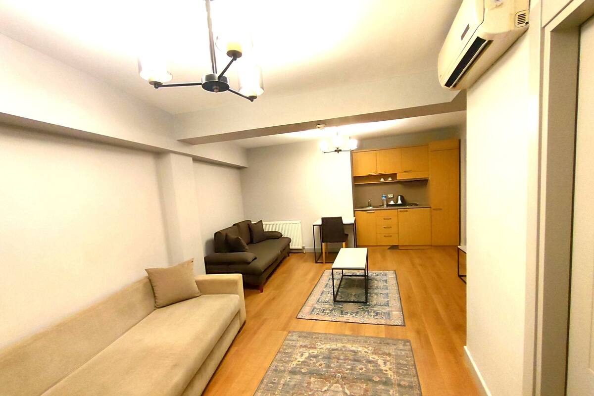 A compact living space with a sofa, a small table, a chair, and a kitchen area with cabinets and a countertop.