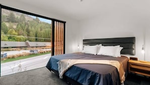 Une chambre à coucher moderne avec un grand lit, une tête de lit et une vue sur une route et des arbres.