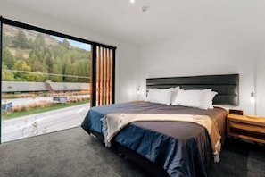 Une chambre à coucher moderne avec un grand lit, une tête de lit et une vue sur une route et des arbres.