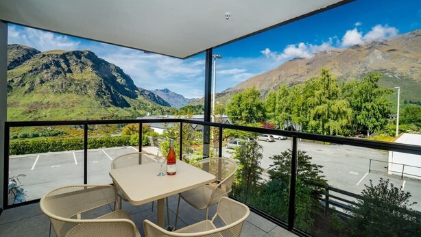 A balcony with a table and chairs, a bottle of wine, and a view of mountains and a parking lot.